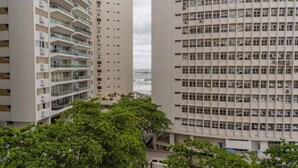 A high-rise building with multiple balconies, a view of the ocean, and surrounding greenery. - Apto c Piscina, Garagem e Academia a 180m da Praia (Guarujá)