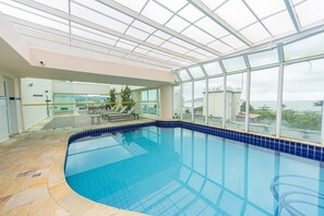 Ein Innenpool mit Glasdach, klarem blauen Wasser und Blick auf das Meer.