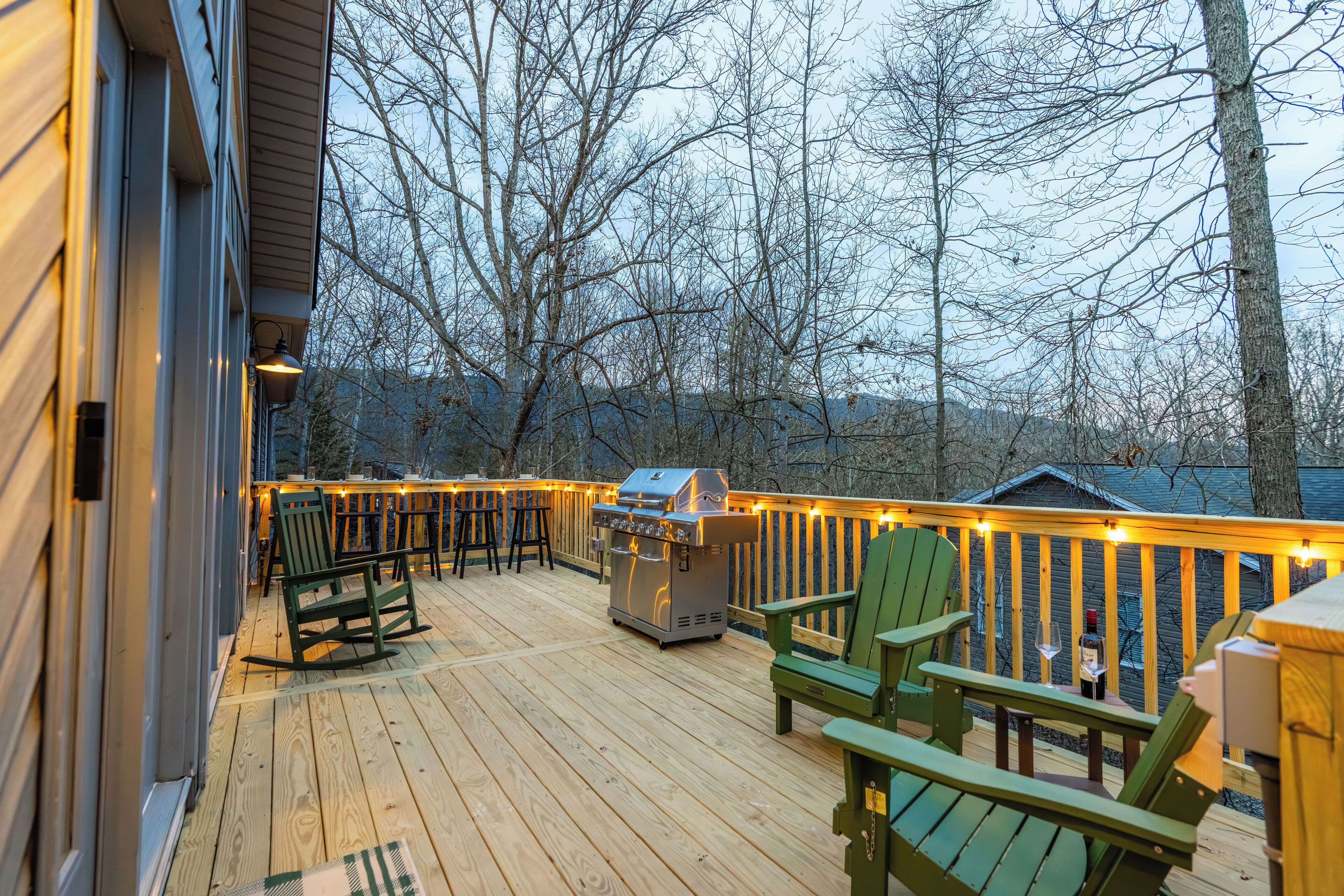 Une terrasse en bois avec des sièges d’extérieur, un barbecue et des guirlandes lumineuses.