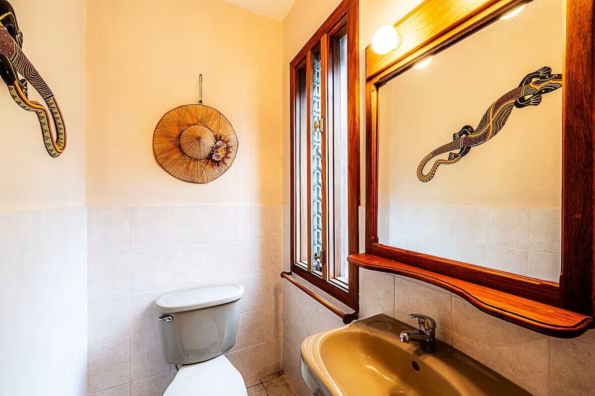A bathroom with a toilet, sink, and decorative wall art including a circular mirror and a lizard design.