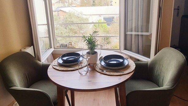 Una habitación con un ventanal grande, una mesa redonda con dos sillas, una planta en maceta y un cuenco.