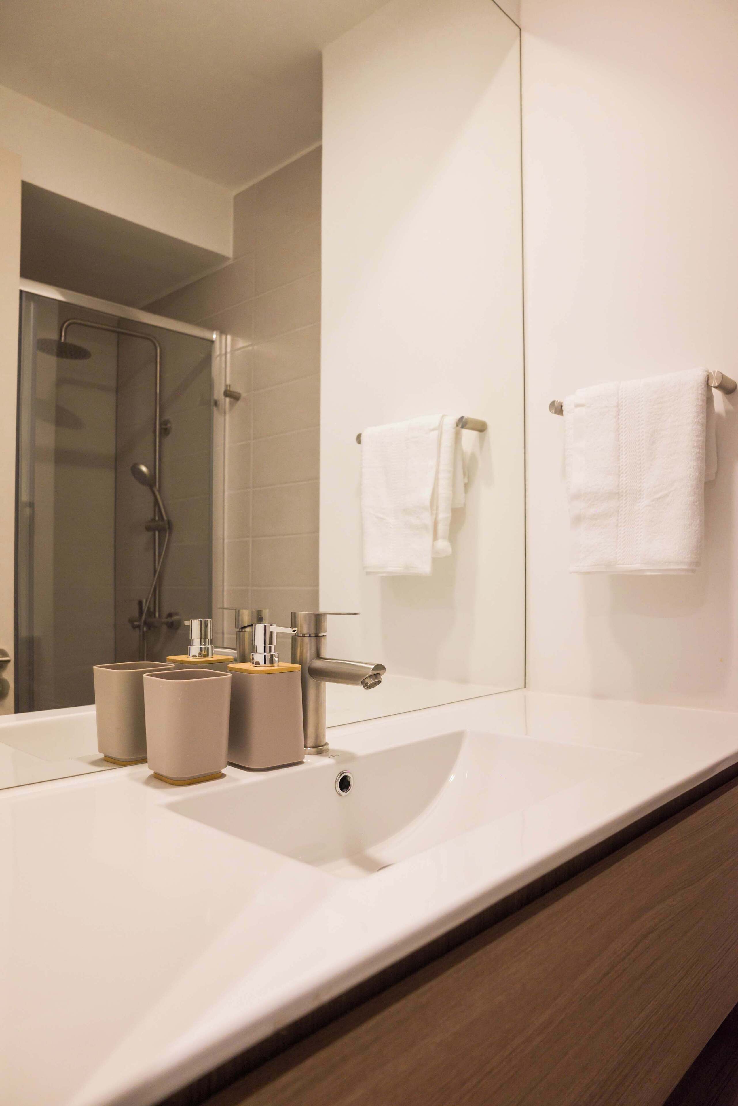 A modern bathroom with a large mirror, two sinks, and a shower.