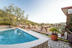 Una piscina amb terrassa de fusta, mobiliari exterior i plantes en testos.