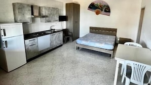 A compact room with a kitchenette, a bed, a dining table, and a chair. - VILLA BERTA (Vieste)