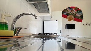 A kitchen with a stainless steel countertop, a modern faucet, a built-in stove, and a wall-mounted TV. - VILLA BERTA (Vieste)