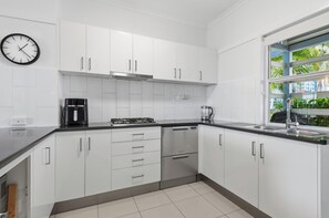 A modern kitchen with white cabinets, stainless steel appliances, and a window with a view of greenery.