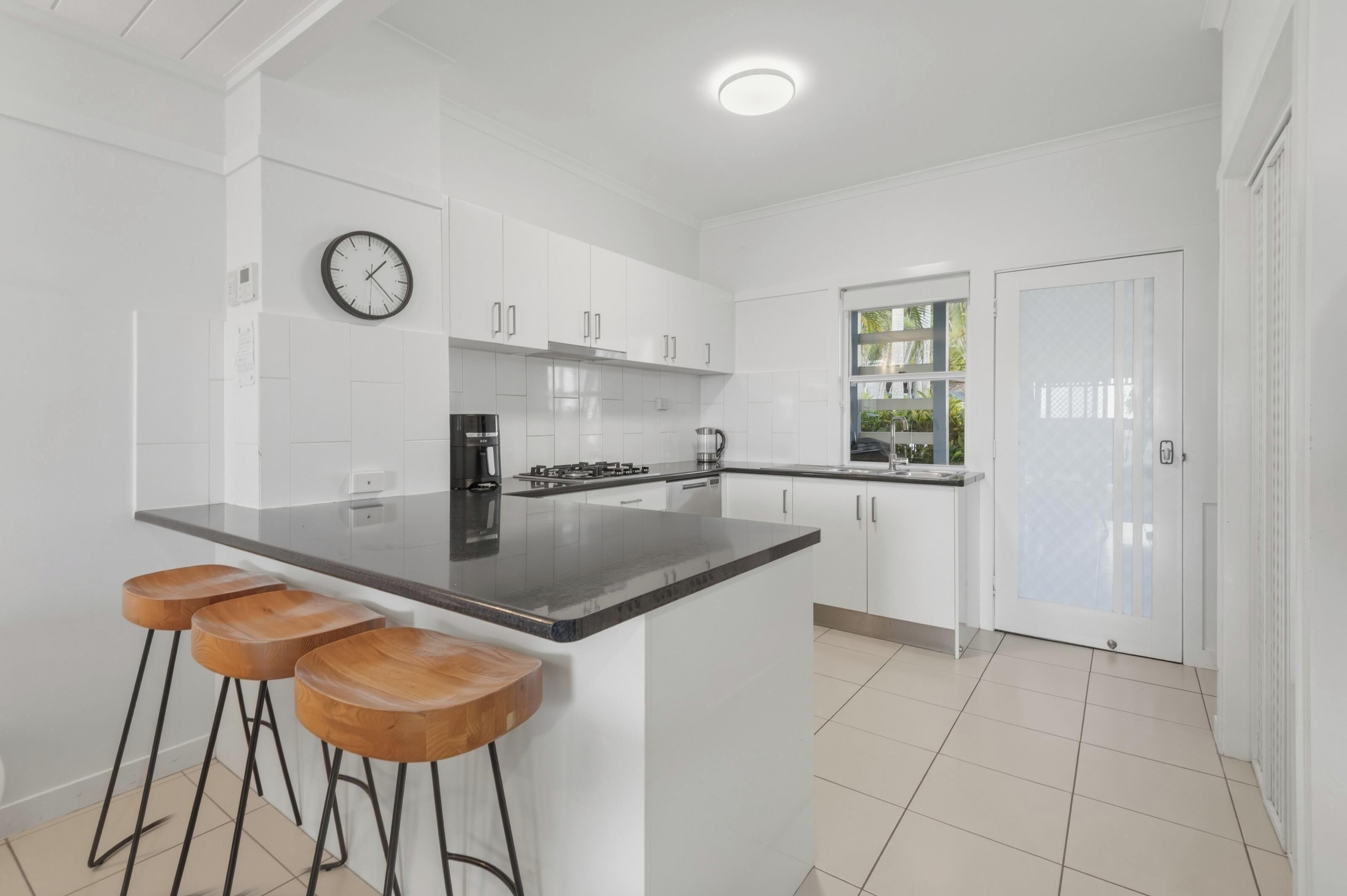 A modern kitchen with white cabinets, a black countertop, and wooden stools.