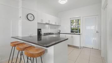 A modern kitchen with white cabinets, a black countertop, and wooden stools.