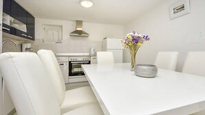 Una cucina moderna con mobili bianchi, forno integrato e un tavolo da pranzo bianco con quattro sedie.