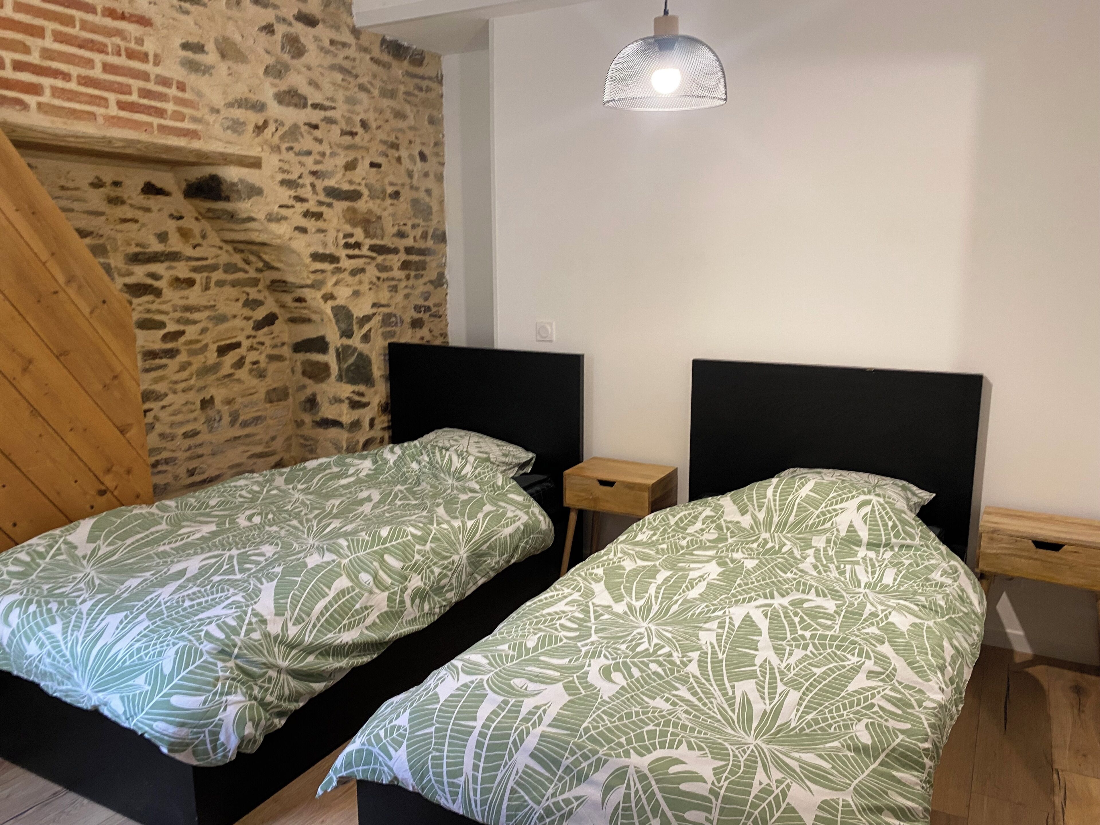 A room with two beds, a stone wall, a wooden sloped ceiling, and a hanging light fixture.