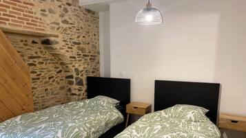 A room with two beds, a stone wall, a wooden sloped ceiling, and a hanging light fixture.