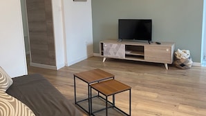 A modern living room with a sofa, a coffee table, a TV on a wooden stand, and a patterned wall. - Apartment Le Pellerin (Le Pellerin)