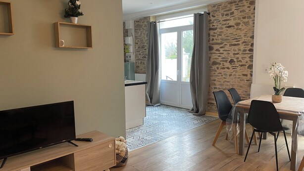A modern living room with a flat-screen TV, wooden furniture, a dining area with a table and chairs, and a kitchen visible through an open door. - Apartment Le Pellerin (Le Pellerin)
