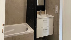 A bathroom with a bathtub, a sink, and a mirror. - Apartment Le Pellerin (Le Pellerin)