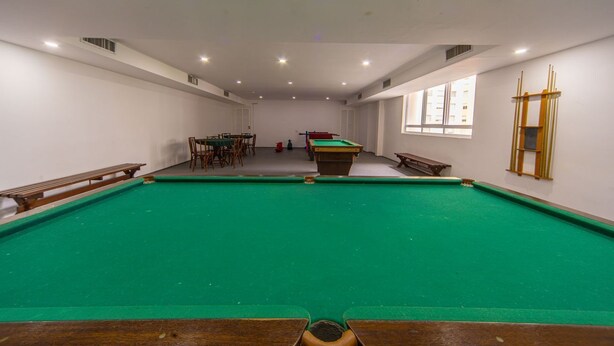 A pool table with surrounding seating, a billiard rack, and a window with a view of buildings. - Apto c Piscina Garagem e Academia a 180m da Praia (Guarujá)