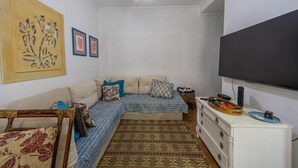 A living room with a sofa, a TV, a ceiling fan, and a decorative wall piece. - Apto c Piscina Garagem e Academia a 180m da Praia (Guarujá)