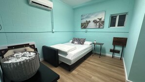 A room with a bed, a small table, a chair, an air conditioning unit, and a painting on the wall. - Casa Brilliance Key Largo Retreat – Family-Friendly 3BR Island Getaway (Key Largo)