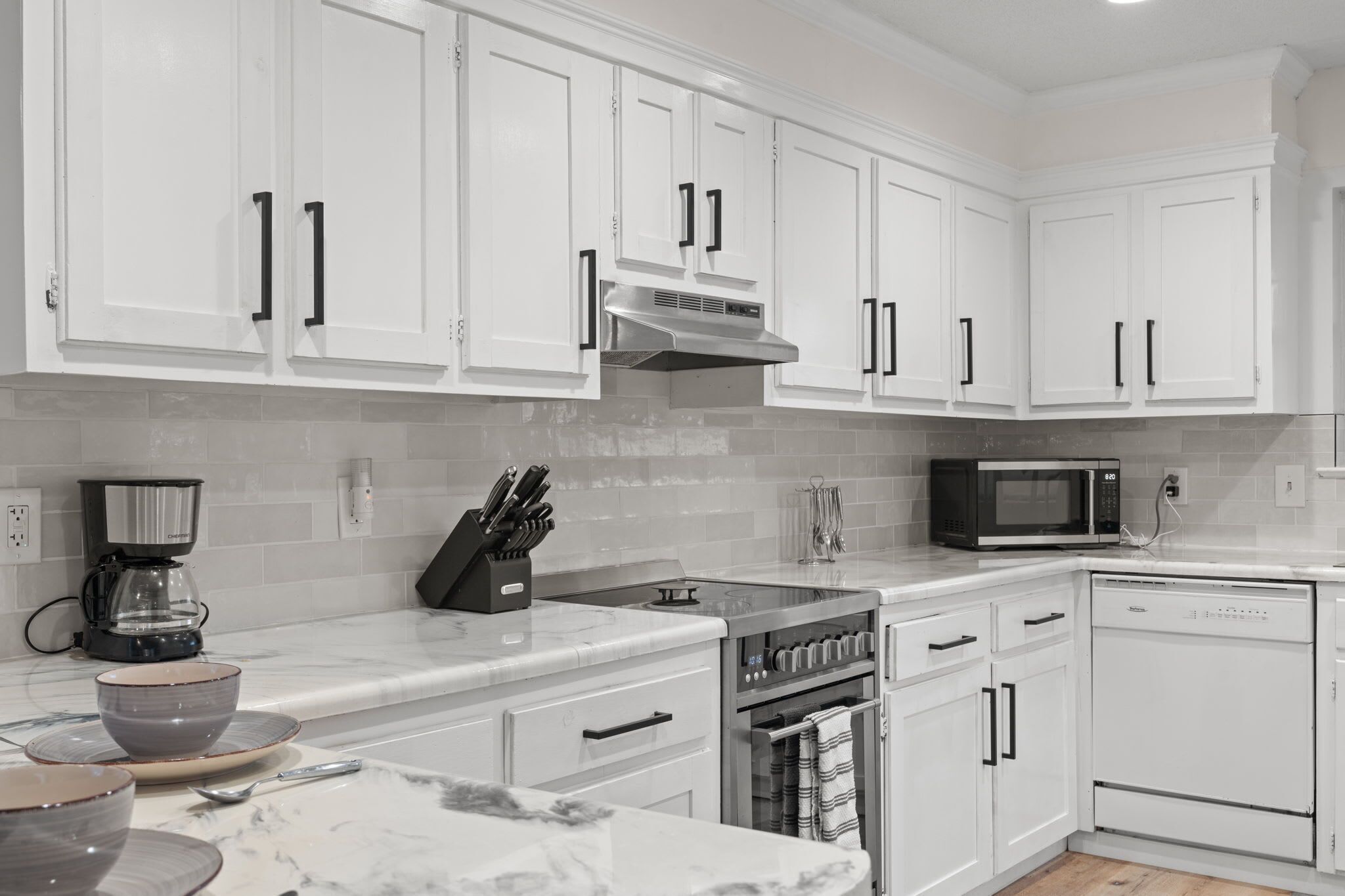A modern kitchen with white cabinets, a built-in oven, a microwave, and a coffee maker.