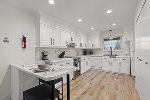 A modern kitchen with white cabinetry, a marble countertop, and a black chair. - The Tanglewood Upper Suite (Chattanooga)