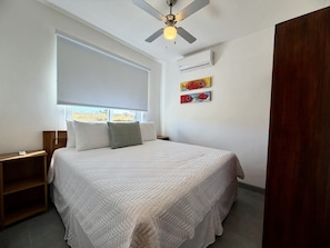 A bedroom with a bed, a nightstand, a ceiling fan, and a window.