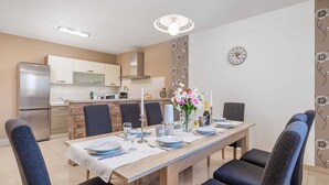 Een moderne eetruimte met een lange tafel voor vier personen, omringd door donkere stoelen. Op tafel staat een decoratieve vaas met bloemen, en er is een wandklok zichtbaar.