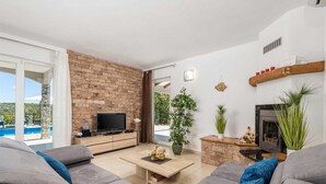 Een moderne woonkamer met een bakstenen muur, een flatscreen televisie, een open haard en uitzicht op een zwembad.