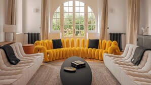 Ein Wohnzimmer mit einem großen Bogenfenster, einem gelben Sofagarnitur, einem schwarzen Couchtisch und einem weißen Sofa.