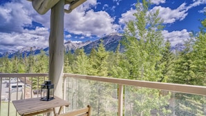 A balcony with a wooden table and chair, overlooking a mountainous landscape with trees and a clear sky. - Spacious Dual-Unit Stay | 2 Addresses | Ideal for Large Groups (Canmore)