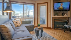 A living room with a sofa, a small table, a TV, and a fireplace. - Spacious Dual-Unit Stay | 2 Addresses | Ideal for Large Groups (Canmore)
