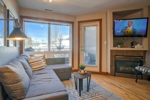 A living room with a sofa, a small table, a TV, and a fireplace. - Spacious Dual-Unit Stay | 2 Addresses | Ideal for Large Groups (Canmore)