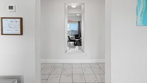 Un couloir doté d’un sol carrelé, d’une reproduction encadrée d’un plan architectural, d’un thermostat numérique et d’un miroir qui donne sur une pièce où se trouvent une baignoire et une chaise.