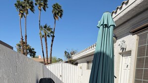 Een terras met kunstgras, een metalen tafel en stoelen, een marineblauwe parasol en een zwarte tas.