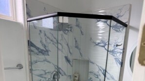 Een badkamer met een douchecabine van glas, een toilet en een wand met marmerlook.