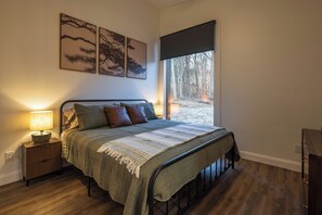 Ein Schlafzimmer mit Bett, Nachttisch und Fenster mit Blick auf Bäume.