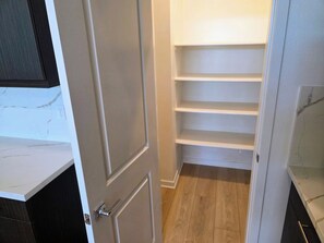 A narrow hallway with a closed door, a white shelf unit, and a wooden floor. - Luxe Desert Escape on the Grove w/ 360° Mountain Views (Palm Springs)