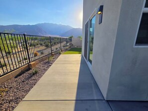 A modern building with a concrete pathway leading to a glass door, surrounded by a metal fence and a gravel bed. - Luxe Desert Escape on the Grove w/ 360° Mountain Views (Palm Springs)