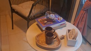 A round table with a white surface and metal legs, a black wicker chair, a book, two mugs, and a box of Hojjat al-Islam cigarettes. - Elegant & Comfortable Apartment with Private Balcony (Santo Domingo Este)
