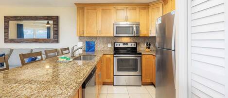A kitchen with granite countertops, stainless steel appliances, wooden cabinets, and a large window.