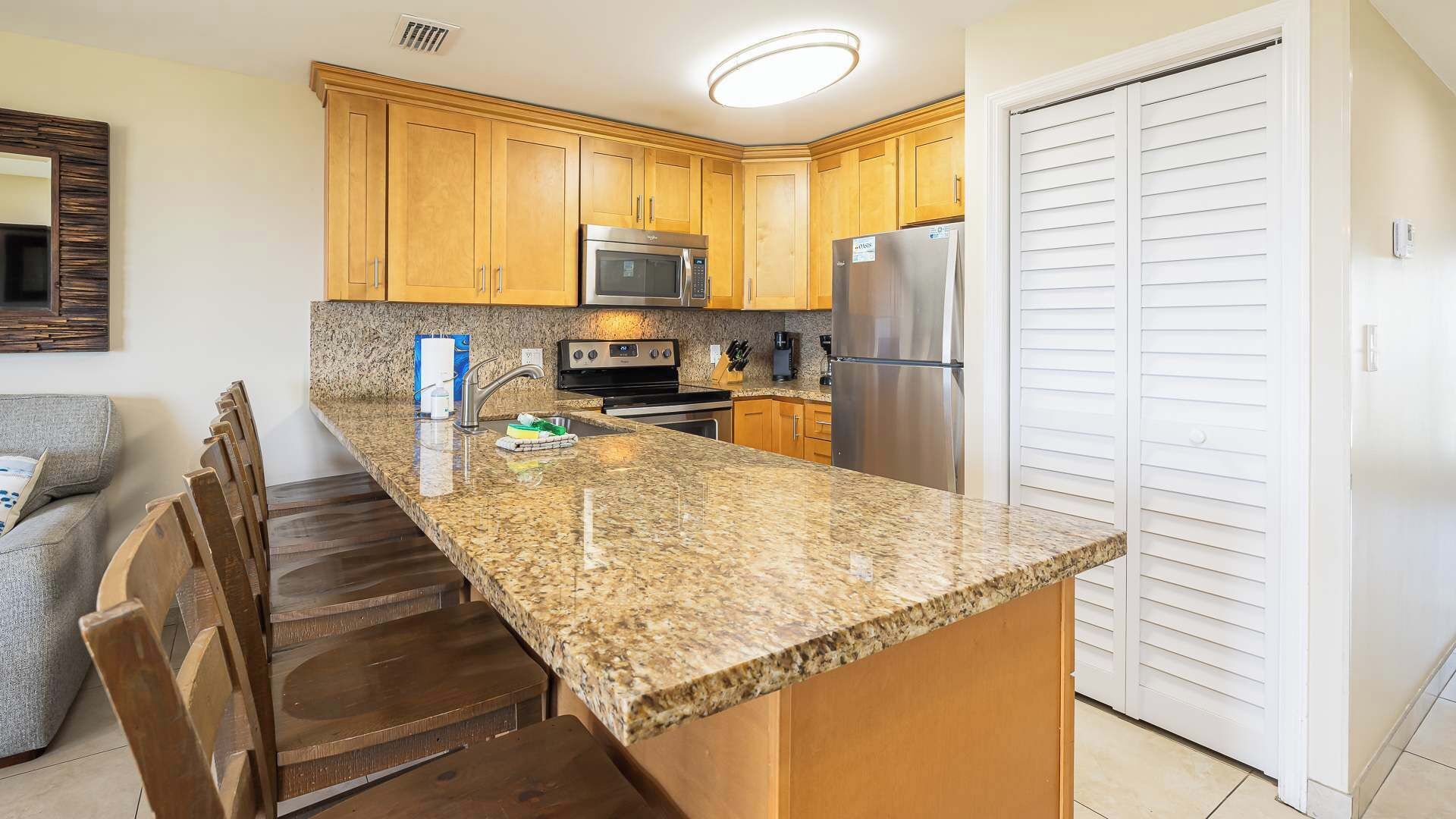 A kitchen with granite countertops, wooden cabinets, stainless steel appliances, and a dining area with wooden chairs.