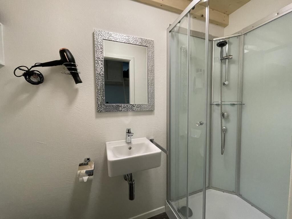 Une salle de bain avec une douche à parois de verre, un lavabo blanc et un sèche-cheveux fixé au mur.