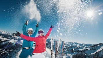 Dos personas esquiando en una montaña nevada con cielo despejado y sol.