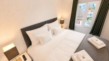 Habitación de hotel con cama, mesita de noche con lámpara, control remoto y ventana con cortinas.