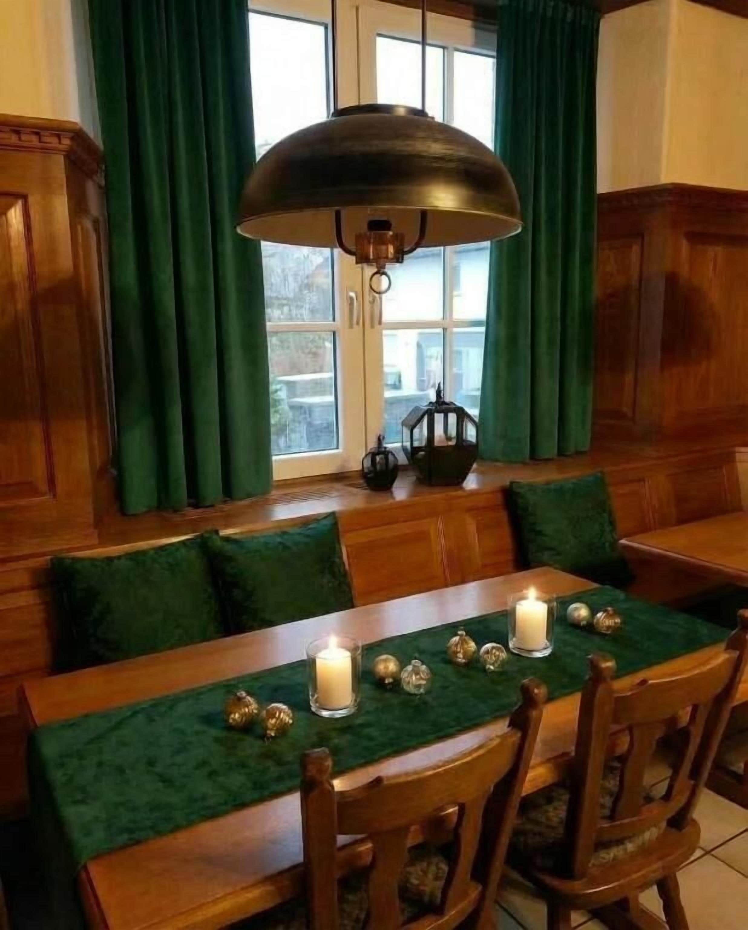A dining area with a wooden table set for four, green curtains, and a large pendant light.