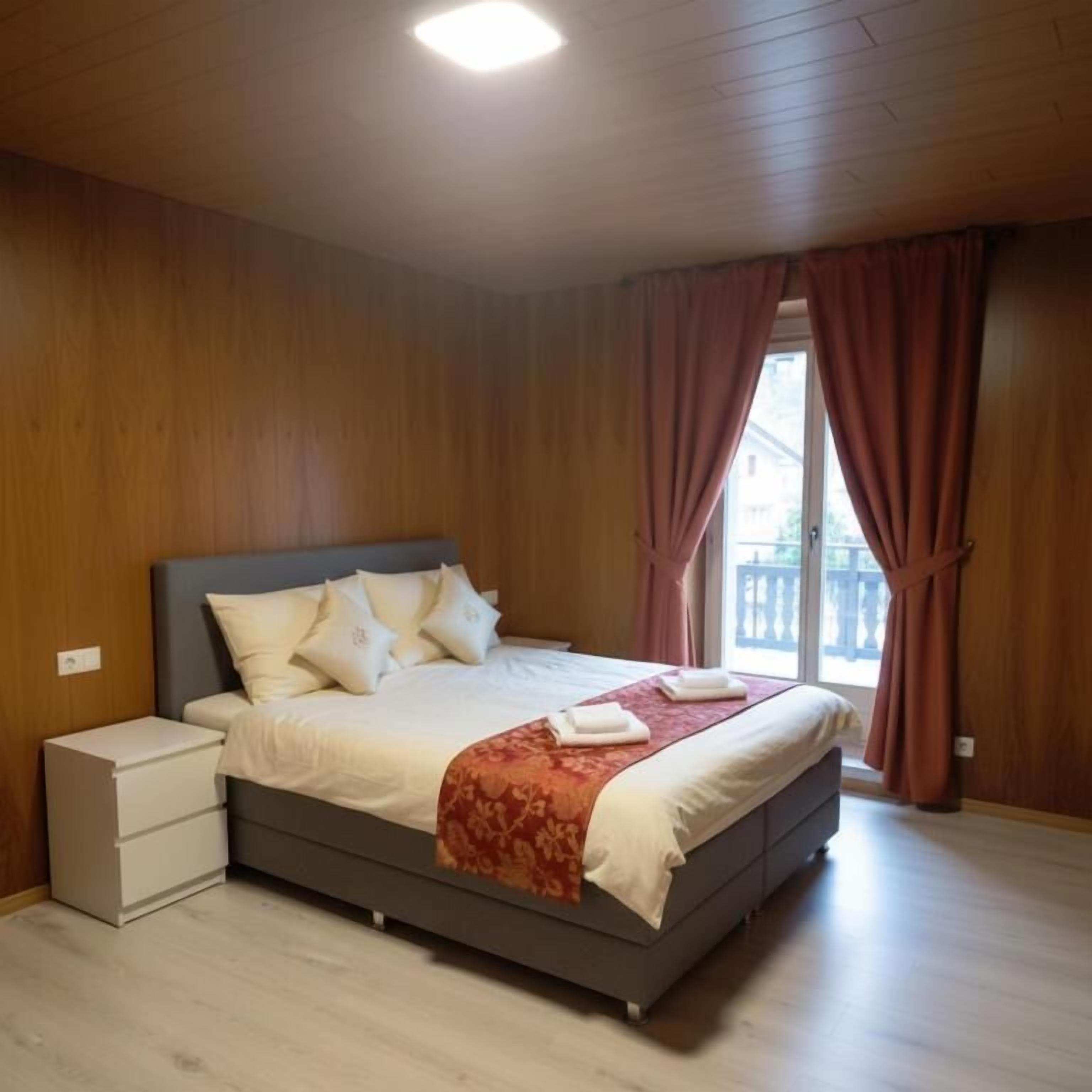 A bedroom with a bed, nightstand, and a window with curtains.