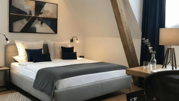 A modern bedroom with a sloped ceiling, a bed with a grey headboard, a bedside table with a lamp, and a desk with a chair. - Hotel Sternen Gurtnellen (Gurtnellen)