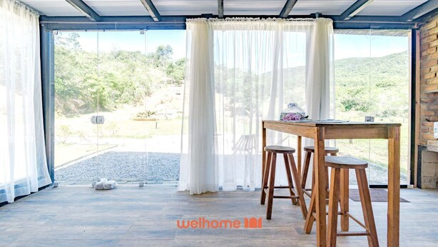 A spacious room with a large sliding glass door leading to a patio. There is a wooden table with two stools and a decorative item on it. The room has a rustic brick wall and a ceiling with exposed beams.
