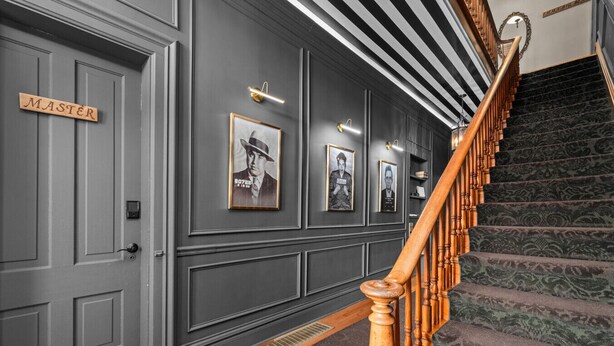 Un couloir avec un escalier en bois, des murs gris et des tableaux encadrés accrochés au mur.