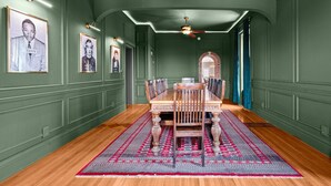 Une salle à manger avec une table et des chaises en bois, des murs verts et un tapis à motifs.