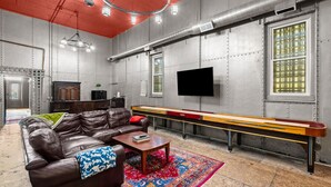 Une pièce avec un canapé en cuir marron, une table basse en bois, un tapis coloré, une table de billard et un téléviseur fixé au mur.