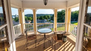 A covered porch with a table and two chairs, overlooking a residential area with houses and greenery. - Elkader Jailhouse Inn (Elkader)